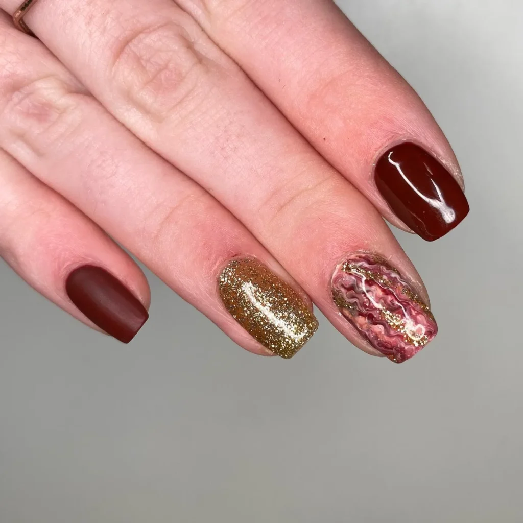 burgundy almond nails with gold foil accents near the cuticle