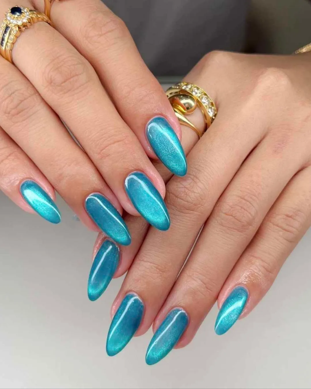 Turquoise blue chrome cat-eye long almond nails with a magnetic shimmer finish