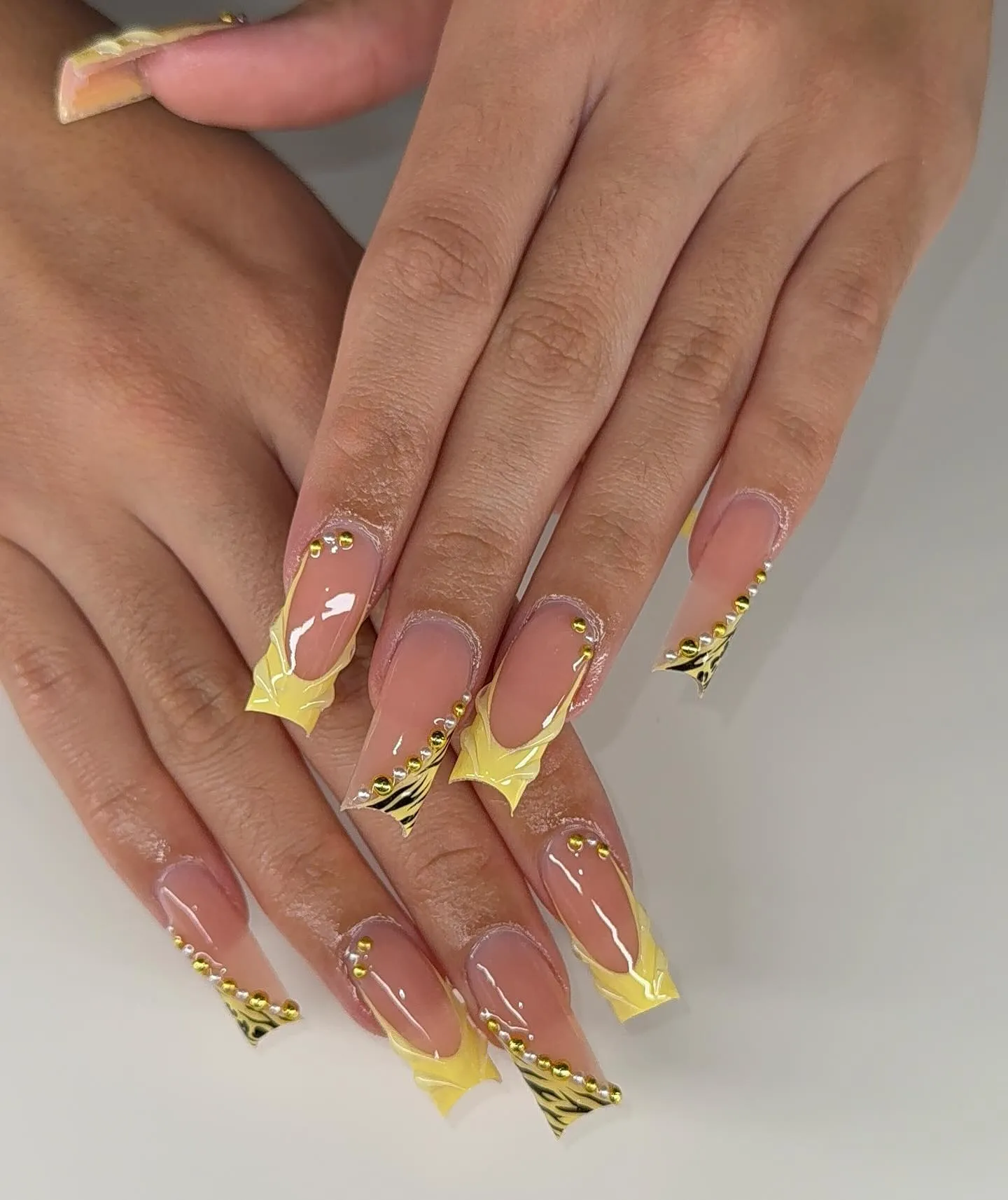 Long coffin nails with nude base, yellow abstract swirl line art, and gold caviar bead accents