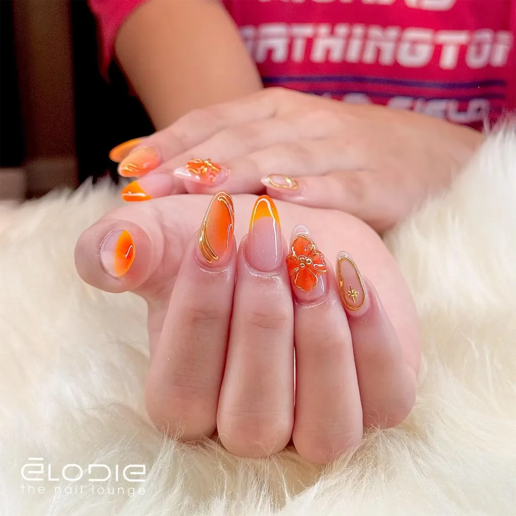 vibrant orange almond nails loaded with 3D floral embellishments and gold swirl linework