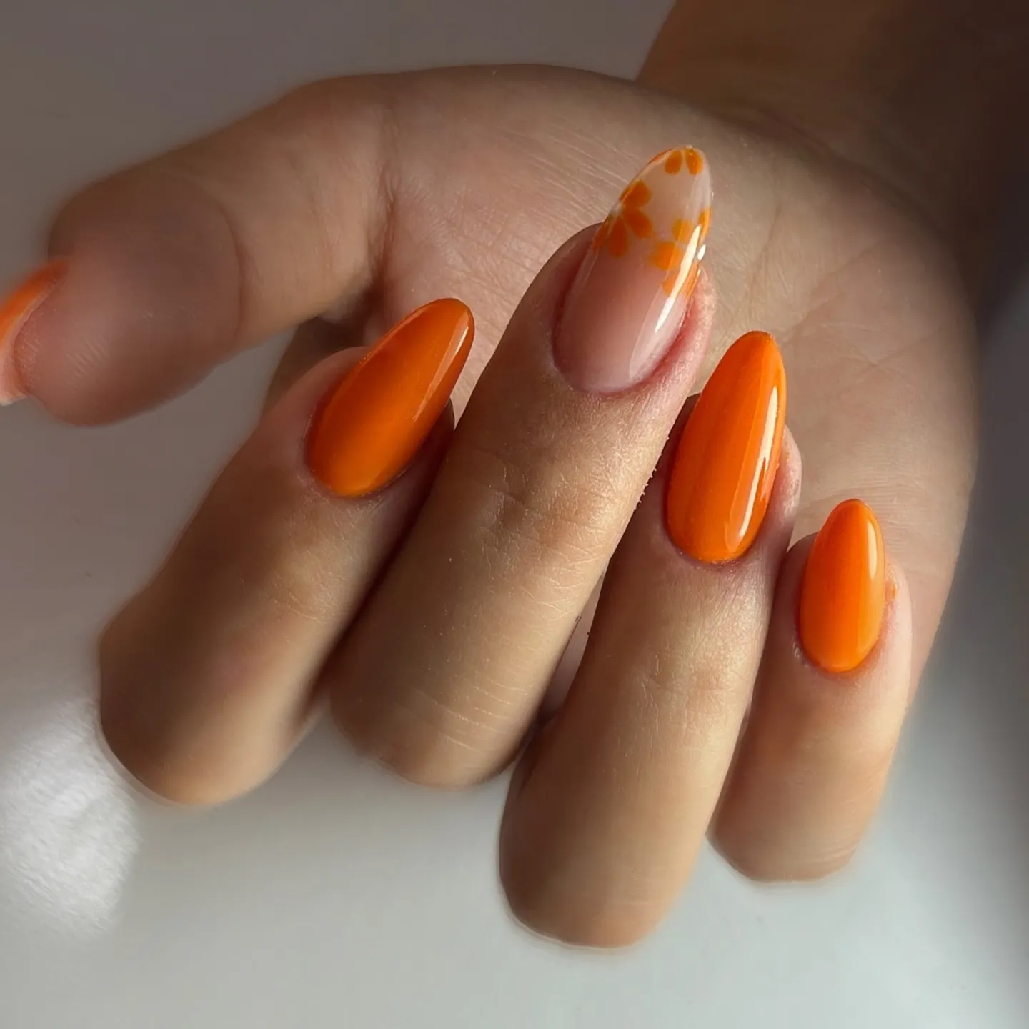 high-gloss orange almond nail look with one hand-painted floral accent nail