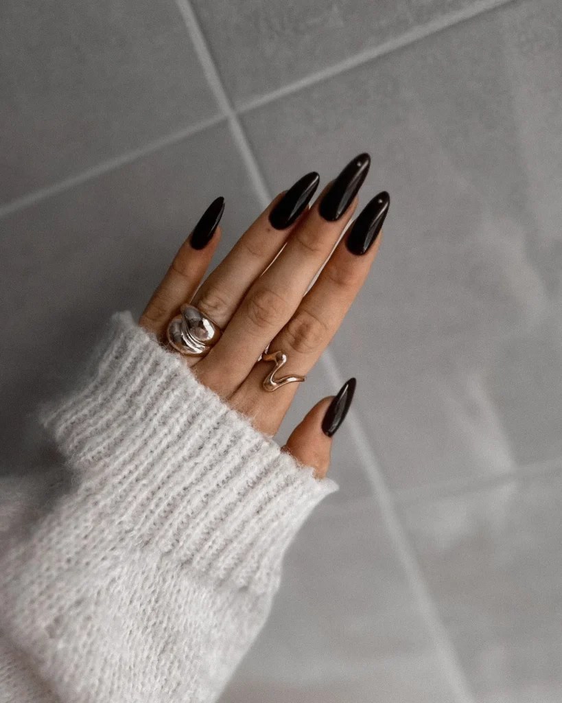 classic glossy black long almond nails with layered gold and silver rings