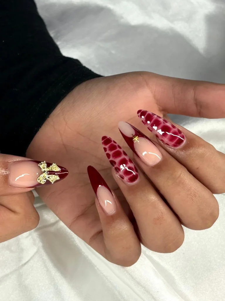 burgundy snake print almond nails with nude French tips and a gold foil charm