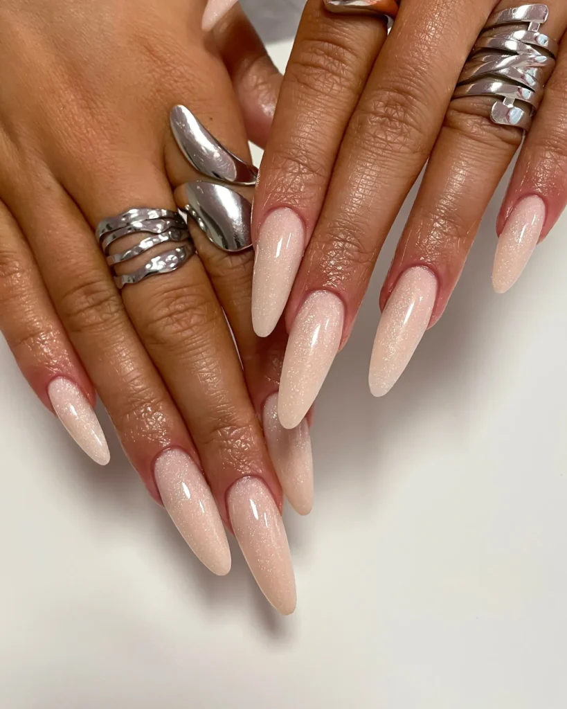 glossy nude pink shimmer long almond nails with a clean girl aesthetic and silver statement rings