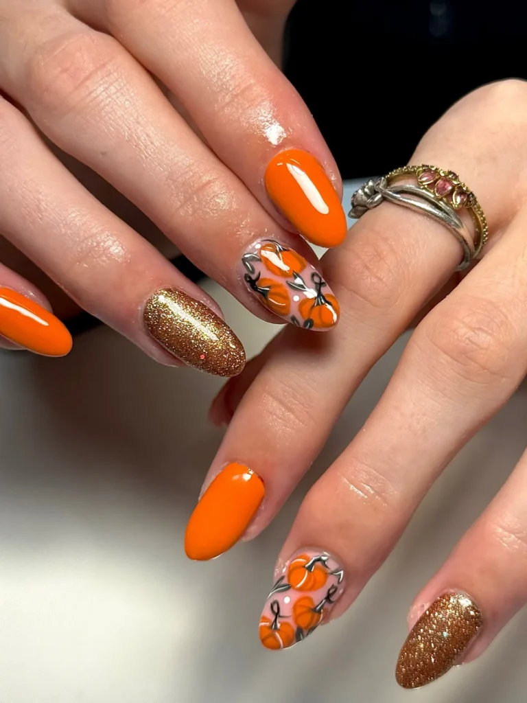 orange almond nail look with gold glitter tips and a hand-painted pumpkin accent nail