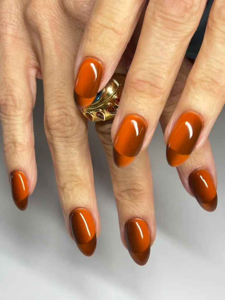 rich brown-to-orange ombre almond nails with a delicate gold ring accent