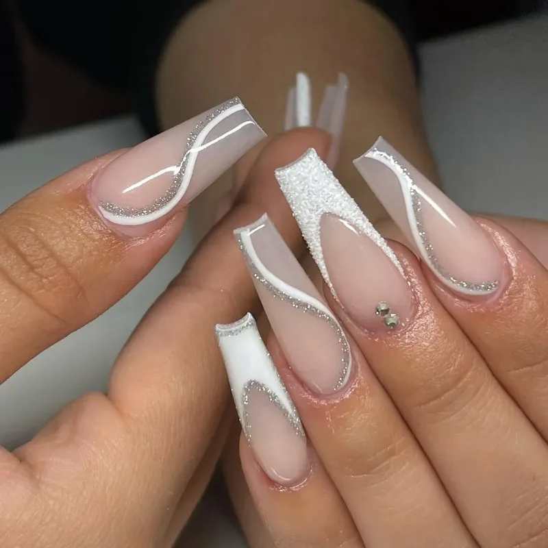 Long coffin nails with white swirl lines, white tips and a small rhinestone