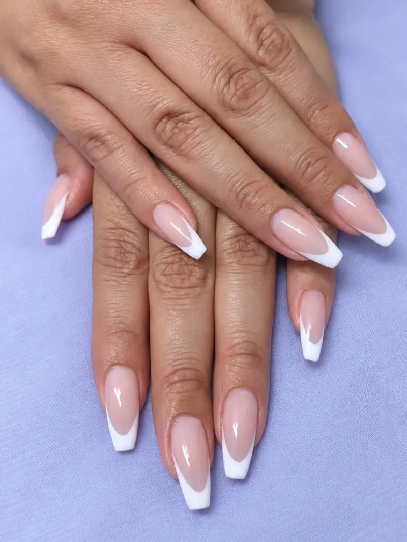 Long coffin nails with a sheer pink base and white French tips on a lavender background