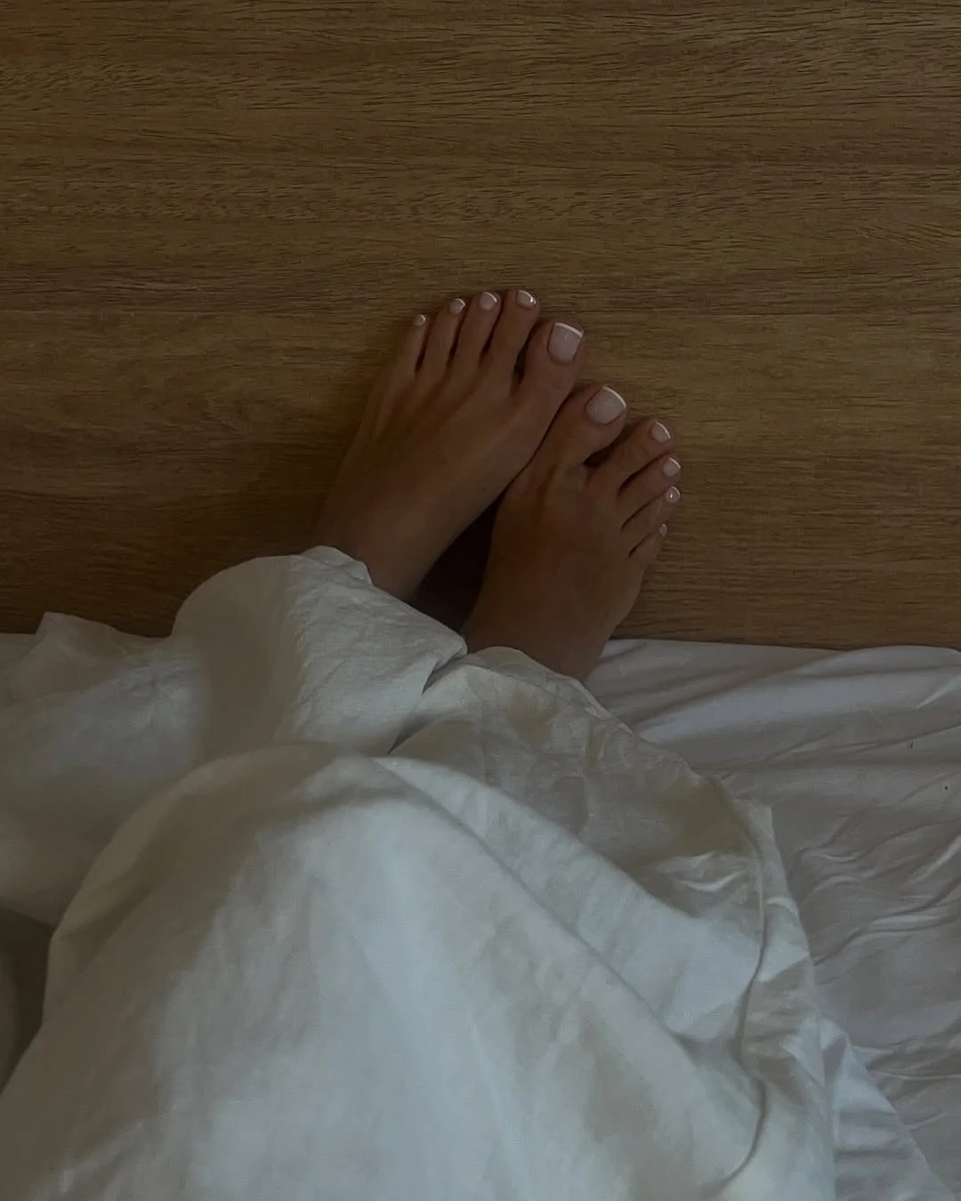 Minimal nude pedicure on bare feet against white linen
