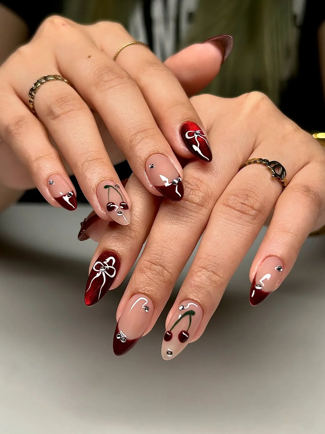 Burgundy and nude almond nails with single cherry art and bows