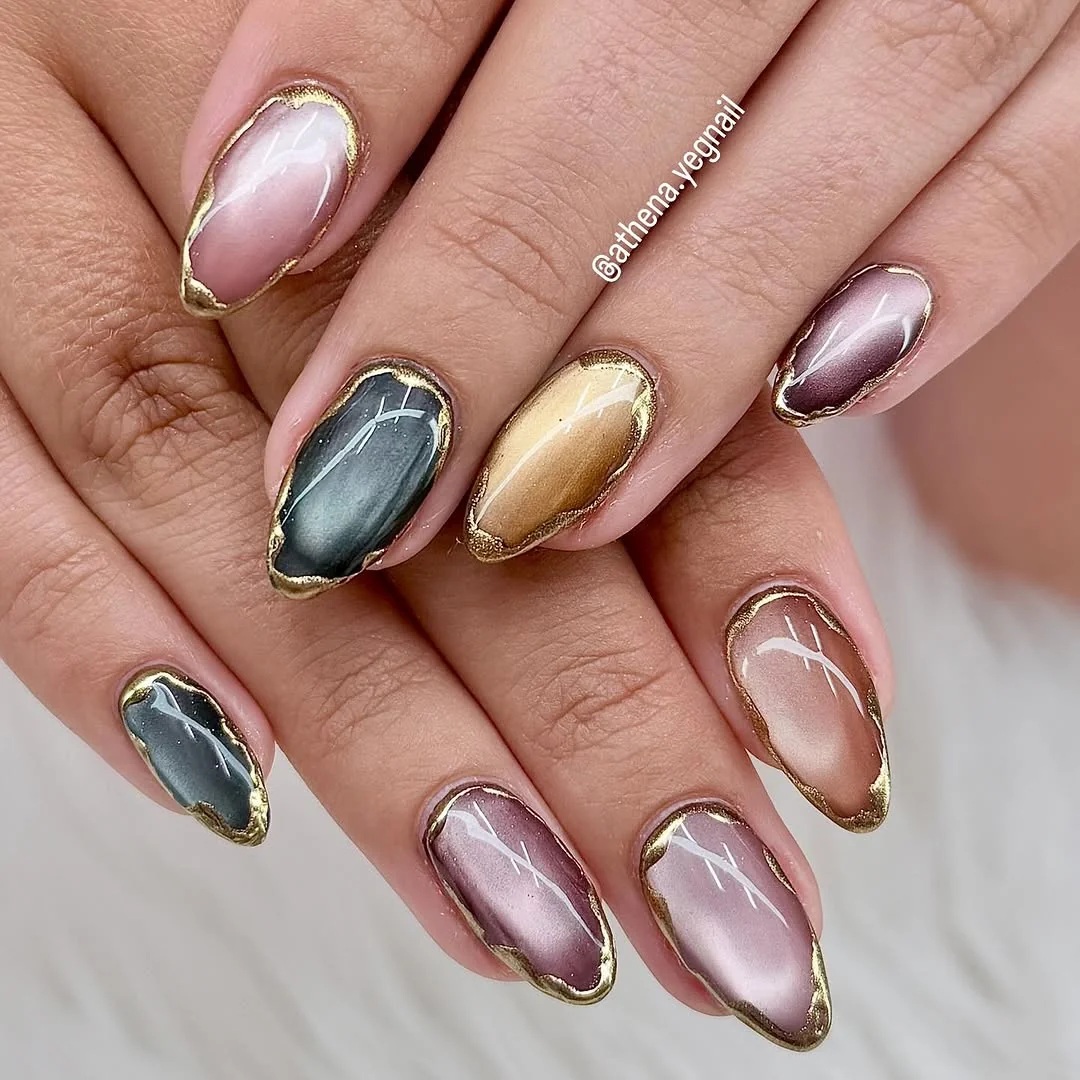 Almond nails with gold foil outlines and gray, gold and mauve cat-eye centers