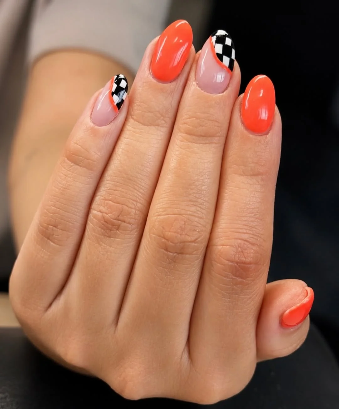Short almond nails in bright orange with a black and white checkerboard accent nail