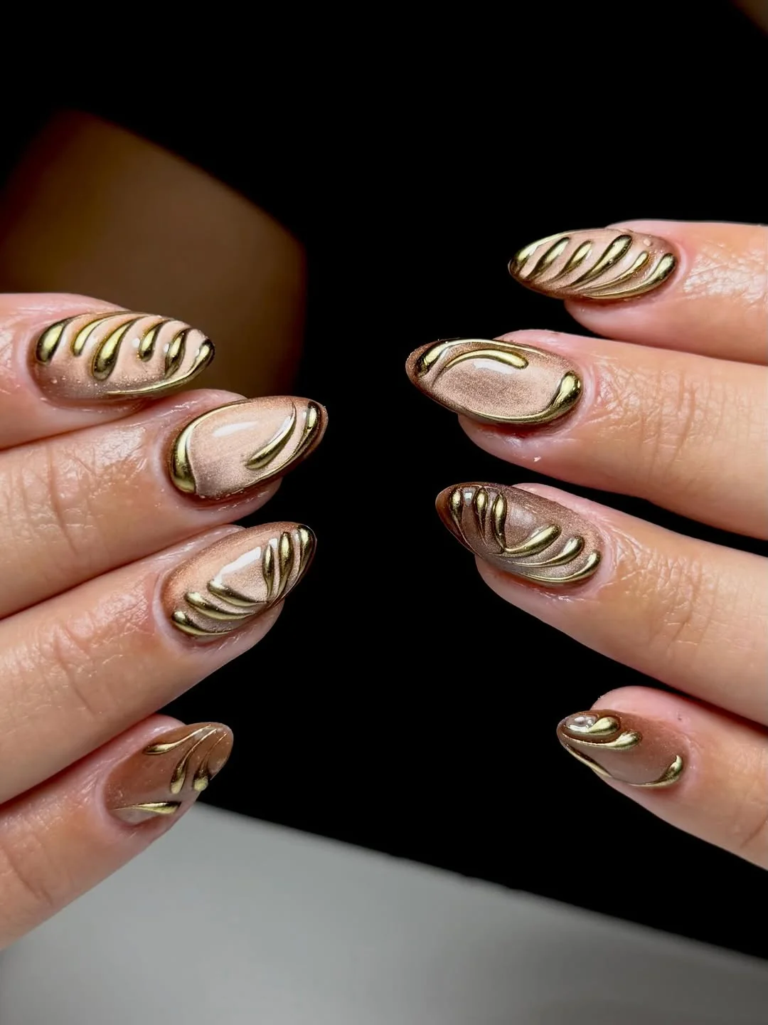 Nude almond nails with 3D gold chrome swirl and cat-eye detail