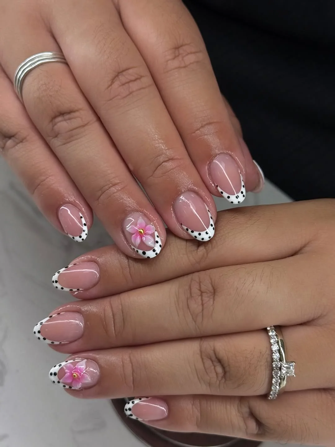 Short nude nails with black and white polka dot tips and flower art
