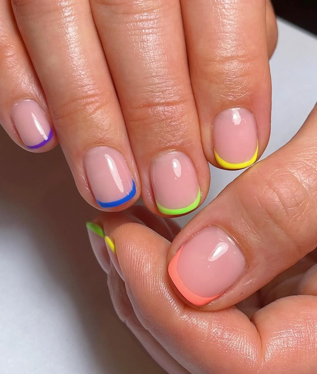 Short nude nails with rainbow micro French tips in blue, yellow and neon orange