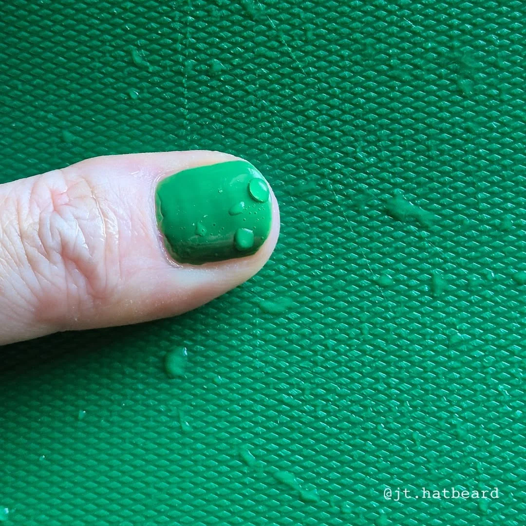 Single short nail painted forest green on a green background