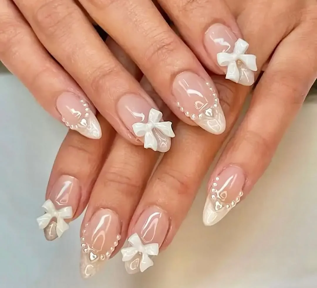 Nude almond nails with 3D white bows and pearls