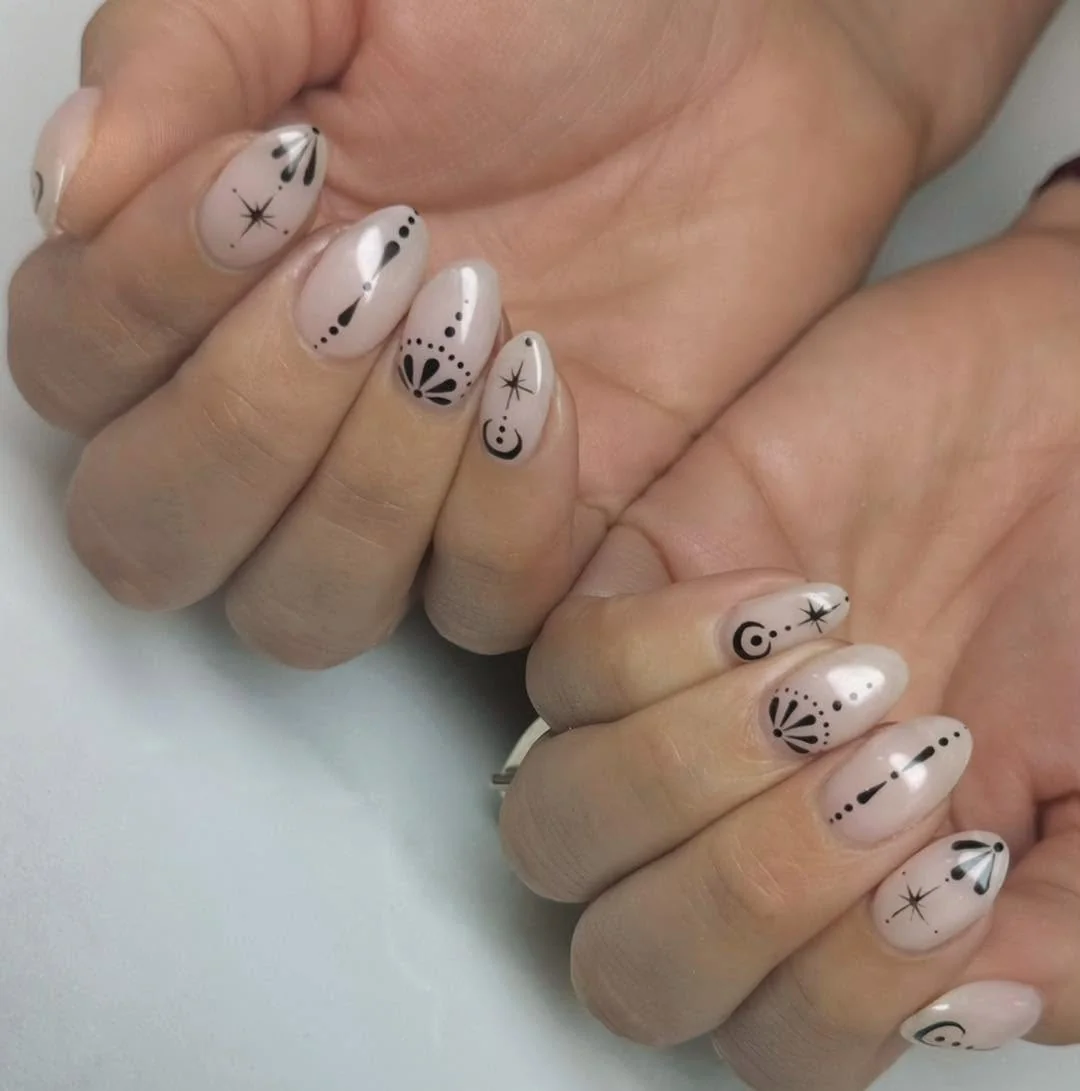 Sheer nude almond nails with black line art charms and stars