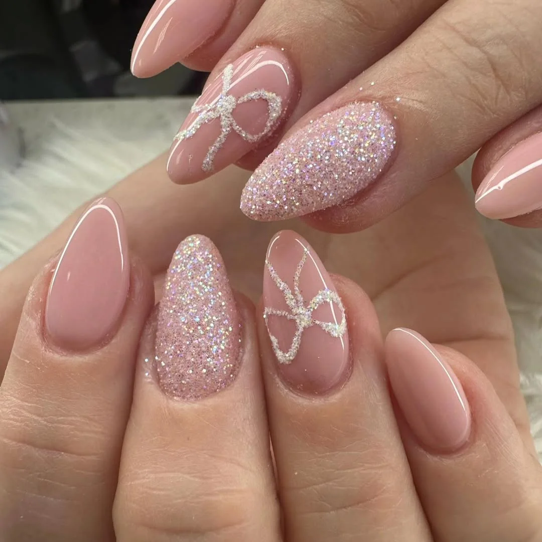 Nude almond nails with glitter accent nails and glittery white bow outlines