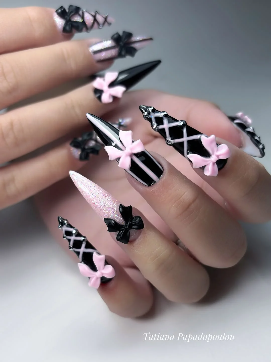 Black stiletto nails with white lace-up lines and pink 3D bows