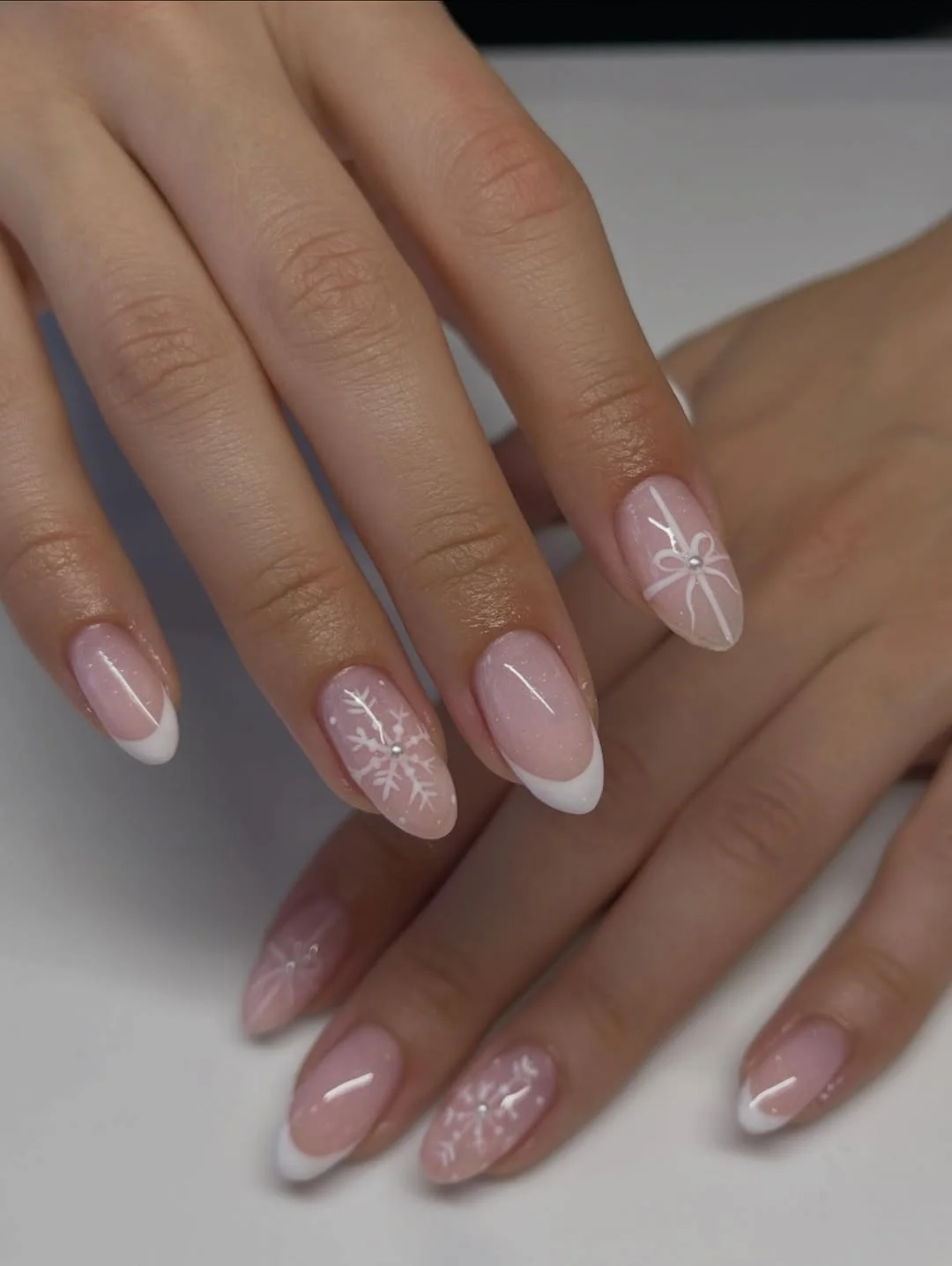 Sheer pink almond nails with white French tips and snowflake detail
