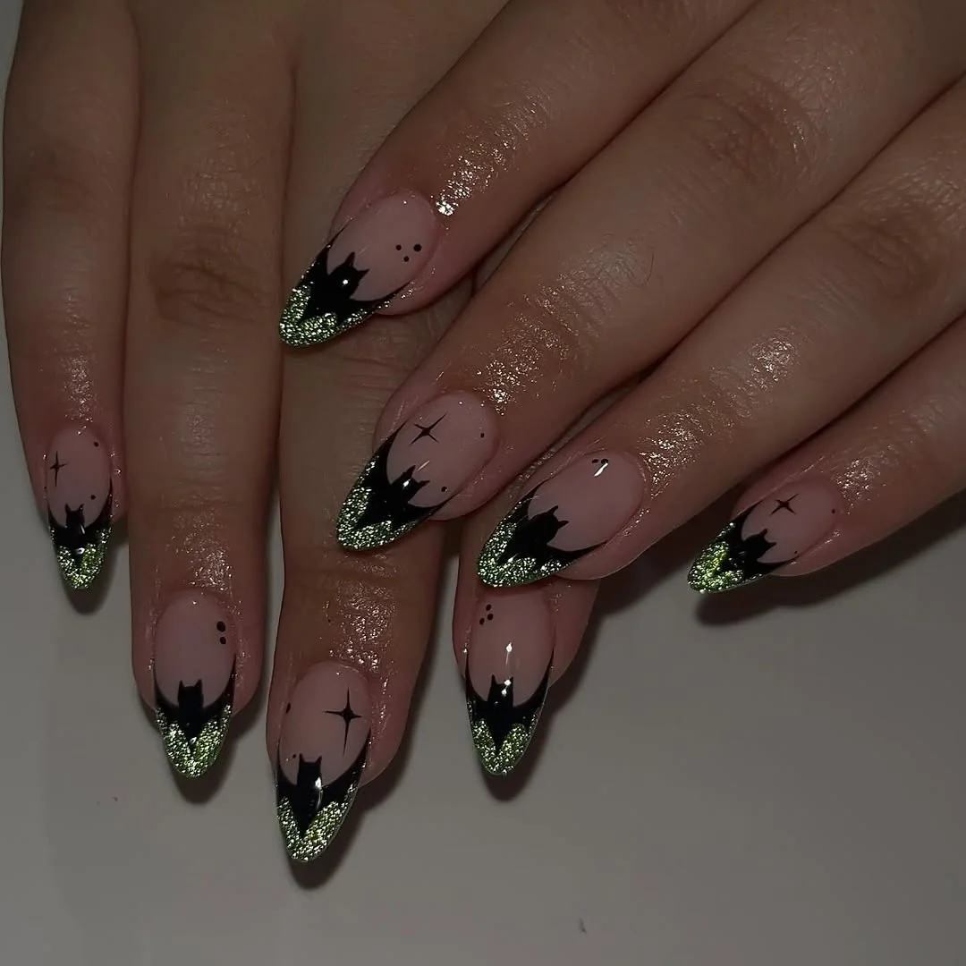 Sheer nude almond nails with black bat French tips and green glitter
