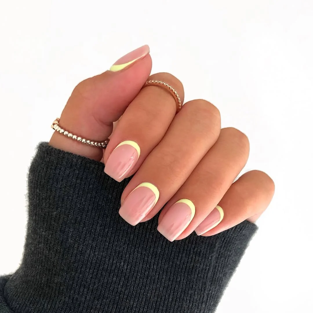 Short nude nails with reverse pastel yellow French curve tips