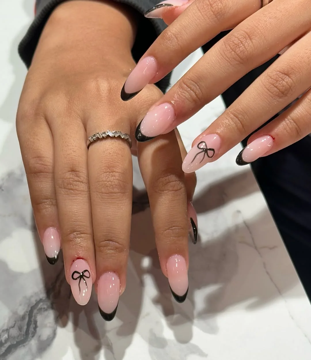 Nude almond nails with black French tips and black bow accents