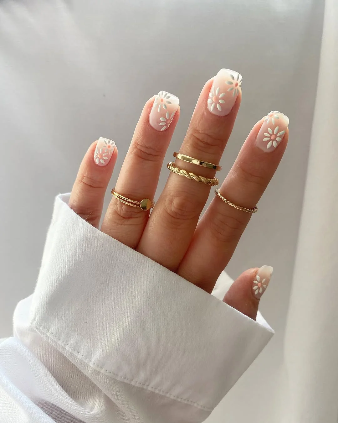 Short nude nails with white French tips and tiny daisy accents