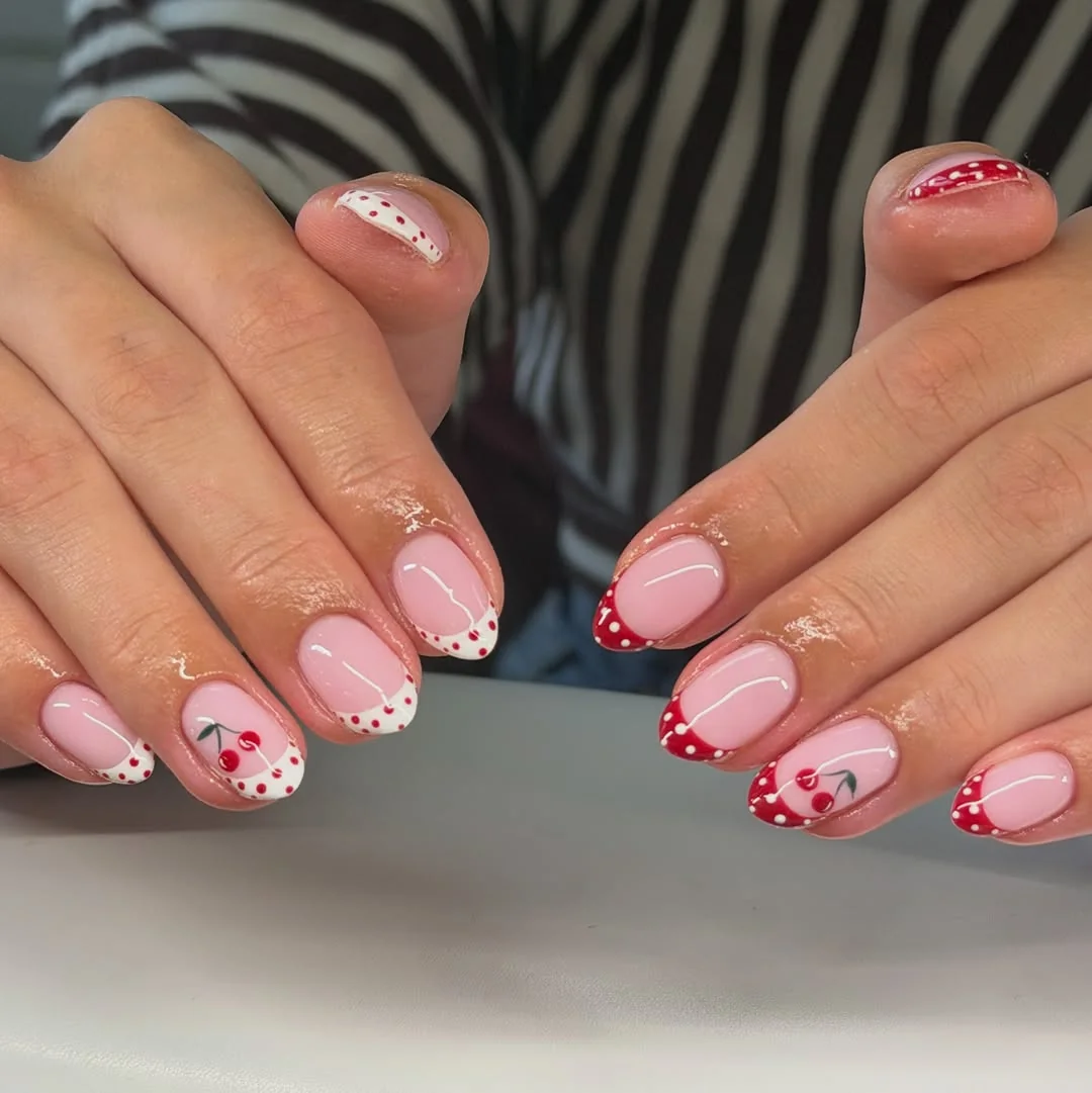 Short pink French tip nails with red polka dots and cherry accents