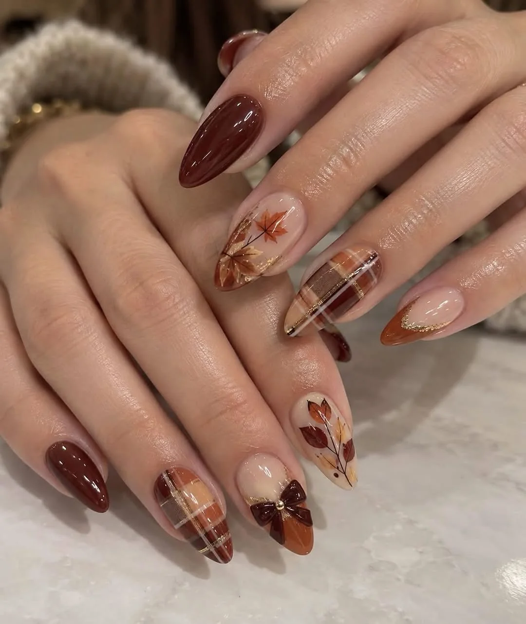 Almond nails with fall leaf, plaid and bow art in brown tones