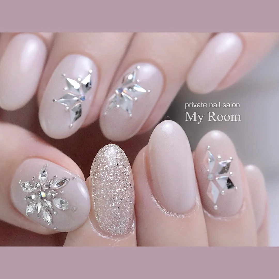 Pale pink nails with rhinestone snowflake centers and glitter accent