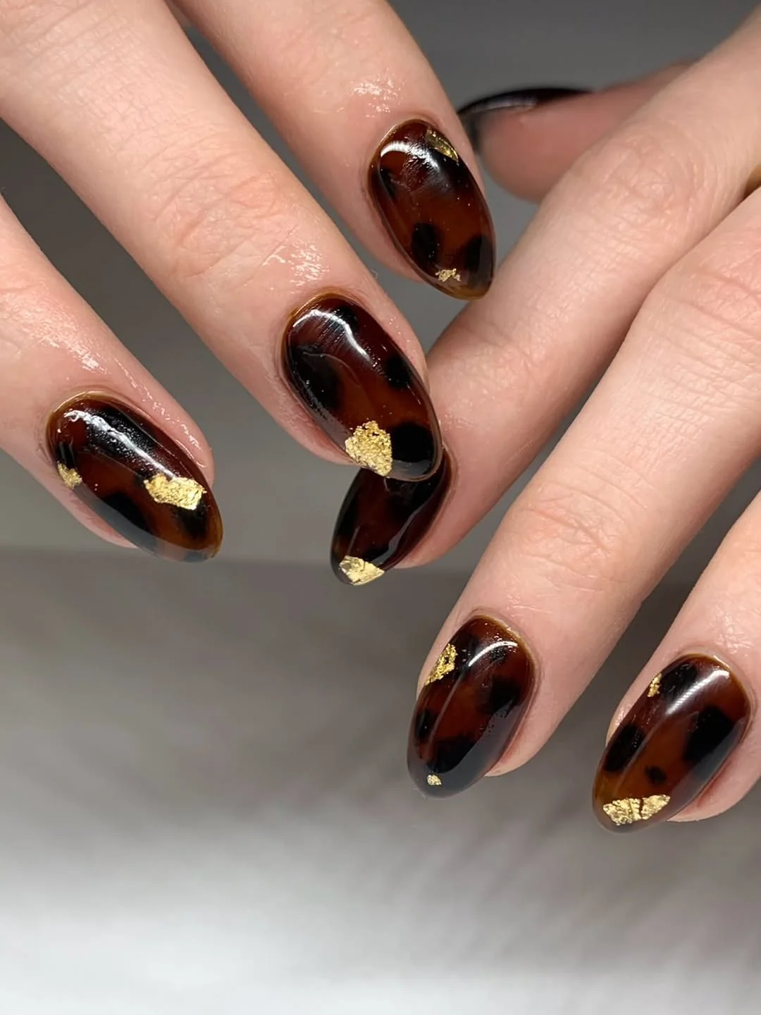 Dark tortoiseshell almond nails with gold foil flakes