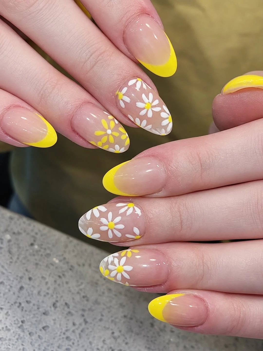 Sheer almond nails with yellow French tips and white daisies